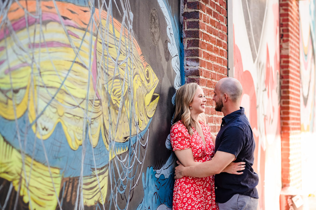 A couple is standing facing each other, leaning against a mural at Fishtown in Philadelphia. They are taking engagement photos.